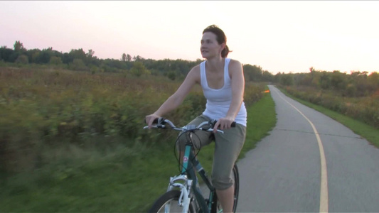 夕阳下一位年轻女性在公路上骑着自行车视频