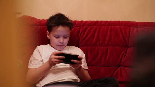 少年在沙发上玩他的便携式游戏机视频