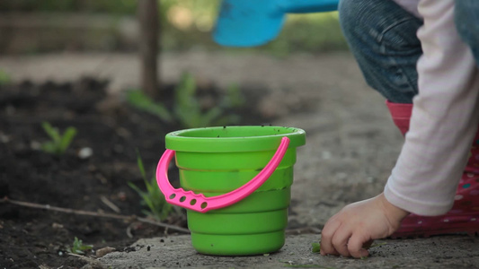小女孩拿着铲子和水桶在后院玩视频