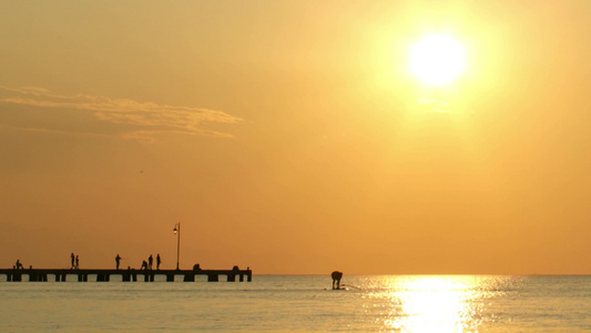 人们在日落时在平静的海洋上风帆冲浪或帆板航行视频