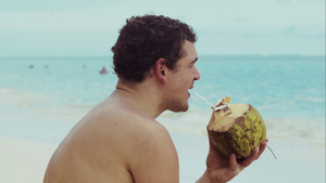 年轻的外国男性坐在海滩上喝椰子汁29秒视频
