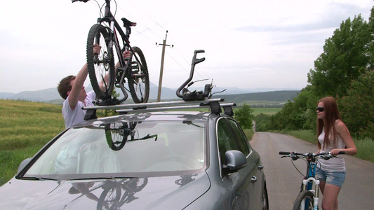 旅途中的男女把放在汽车顶上山地车搬下来视频