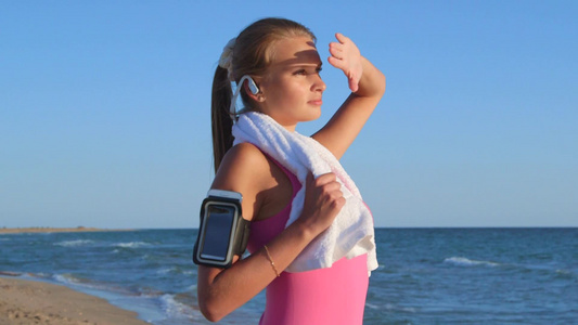 健身运动女孩戴着无线耳机在海滩欣赏日落[戴起]视频