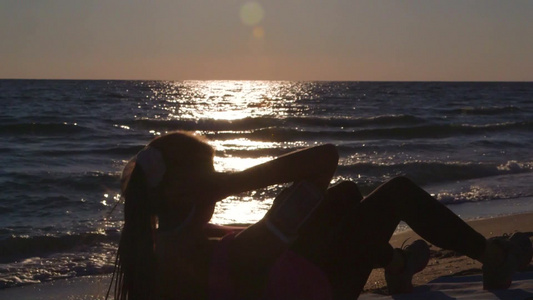 日落沙滩上运动美女卷腹锻炼视频
