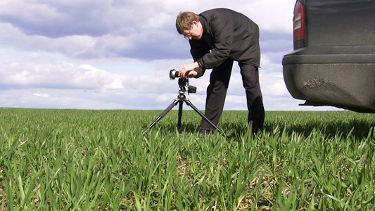 摄影师在草地上架起三脚架相机准备拍摄风景视频