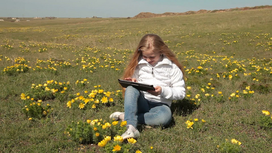 女孩在野生牡丹草地上玩平板视频