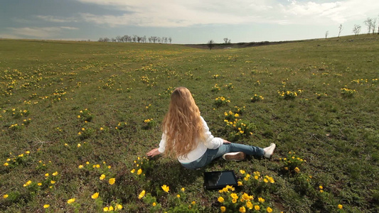 金发女孩坐在开满黄色花朵的草地上视频