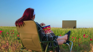 家庭主妇在绿草环绕的野外躺在椅子上看电视20秒视频