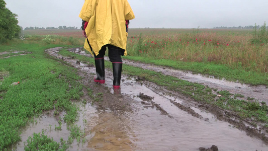 穿着黄色雨衣的农民在雨中穿过田野的一条土路视频