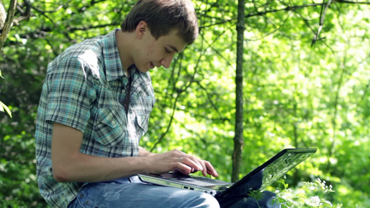 青少年坐在树林里在笔记本电脑上写日志视频