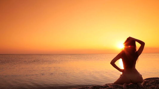 日落时坐在海滩上的女人的剪影[黄昏时候]视频