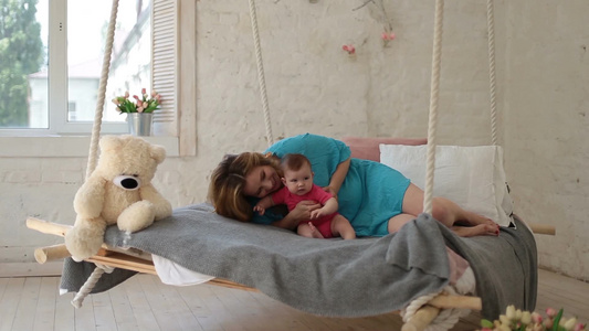 美丽的年轻母亲躺在床上和她可爱的宝贝女儿玩耍[迷人]视频