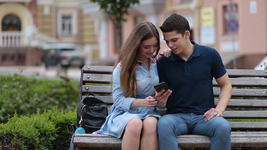 情侣坐在公园长凳上一起玩手机[浓情蜜意]视频