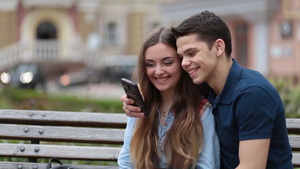 年轻的夫妇坐在长凳上用手机看视频20秒视频