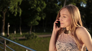 日落时靠在人行桥的栏杆上金发女人使用智能手机聊天33秒视频
