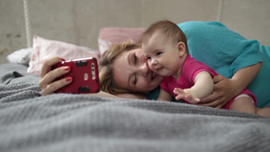 年轻女性和可爱的幼儿躺在床上用智能手机自拍22秒视频