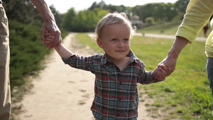 可爱的微笑的小蹒跚学步的男孩的肖像，蓝色的眼睛牵着手，与祖父母在公园散步。 快乐的多代家庭在春天的大自然里玩得27秒视频