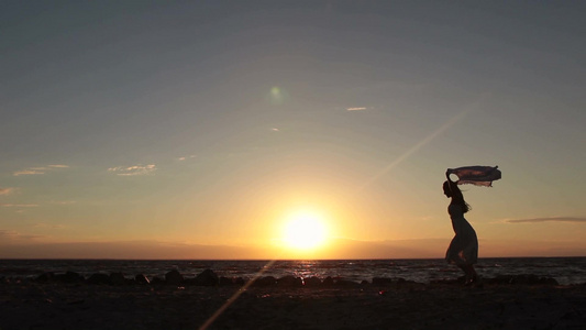 日落时在海滩举起飞扬的丝巾奔跑的女孩剪影视频