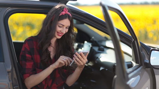 美丽年轻的女人站在汽车旁玩手机视频