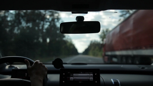 从车辆内部查看女子驾驶汽车在森林的高速公路上超车[车俩]视频