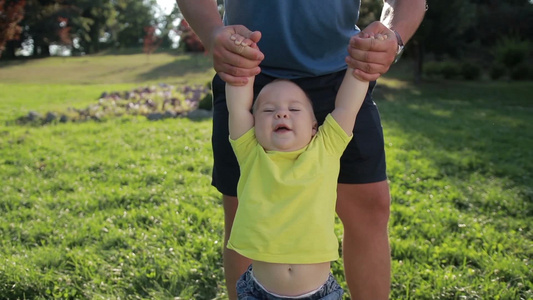 顽皮的父亲在公园里用手摆动他可爱的宝贝视频