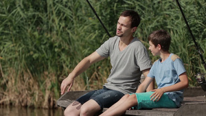 父子坐在湖边木墩上垂钓休闲35秒视频