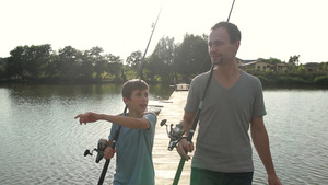 快乐的父亲和兴奋的儿子带着钓竿走在木墩上交谈24秒视频