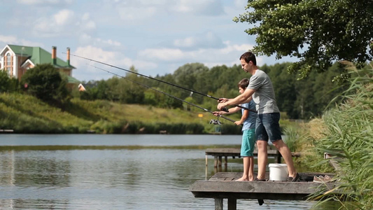 年轻男性和小男孩在湖边的木墩上钓鱼视频