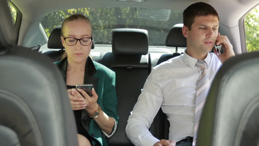 两个商业伙伴在豪华汽车的后座使用手机[品牌手机]视频