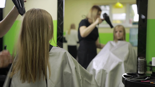 理发店里发型师用吹风机烘干女孩的头发视频
