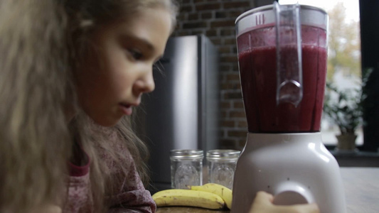 小女孩在厨房里等待搅拌机里制作的新鲜的浆果奶昔视频