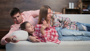 妻子和丈夫还有可爱的女儿在家里一起躺在沙发上用智能手机上网12秒视频