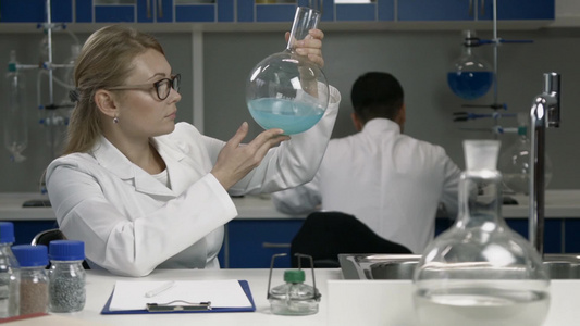 女研究员在化学实验室进行研究瓶子中蓝色液体物质视频