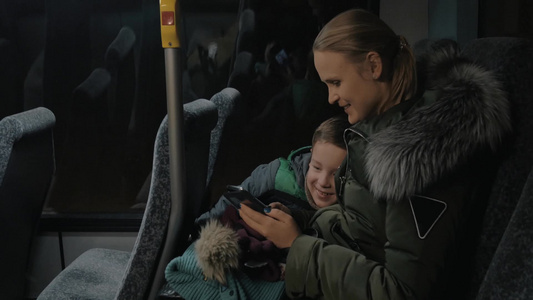 妈妈和儿子晚上乘公共汽车使用手机看照片[品牌手机]视频