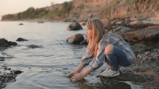 一个小女孩在海边用海水冲洗她的手和脸视频