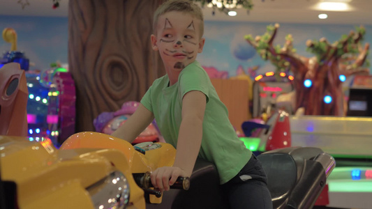 男孩画着猫脸在室内游乐园玩摩托车赛车模拟器视频