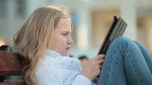 小女孩坐在长凳上玩平板电脑视频
