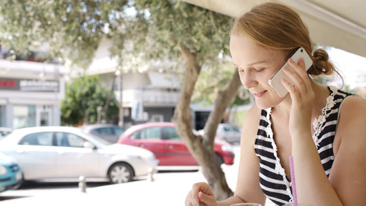 年轻女子坐在露天自助餐厅吃茶点打电话视频