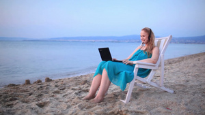 女人坐在海边的躺椅上拿着笔记本电脑戴着耳机交谈23秒视频