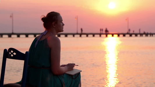 夕阳西下年轻的女人坐在海边写日记视频