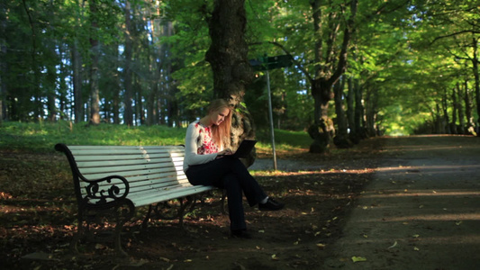 女人坐在公园长凳上使用她的笔记本电脑视频