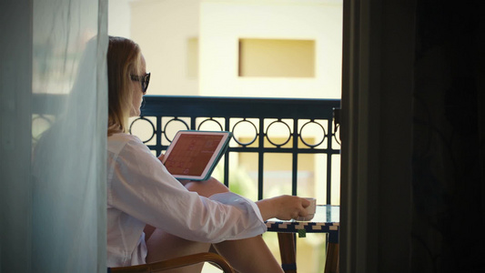 年轻女性使用平板电脑和在酒店阳台喝茶视频