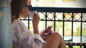 女人在炎热的夏天在露台上用手机发短信和喝茶17秒视频