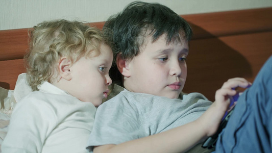 两个年幼的孩子一起在沙发上玩平板电脑视频