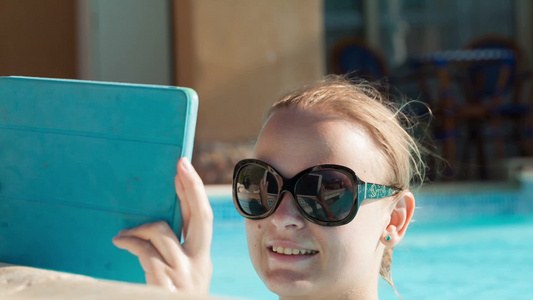 美丽的年轻女人戴着太阳镜用平板电脑在水池里自拍视频