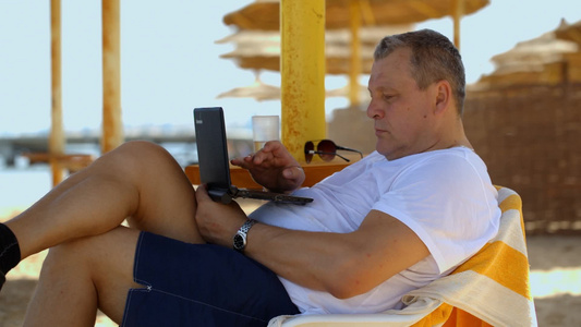男人在海滩度假胜地用笔记本电脑放松娱乐视频