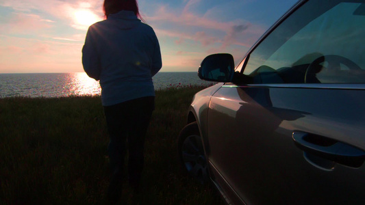 女人离开了汽车在日落时朝海边走去视频