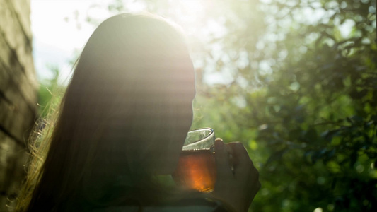 一个年轻女人在日落时喝热茶背影[二十多岁]视频