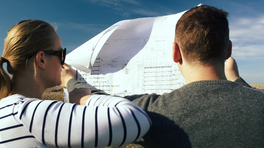 年轻的建筑师打开蓝图在空旷的土地上讨论未来的建筑工程视频