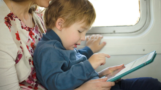 火车上男孩坐在母亲的腿上玩平板视频